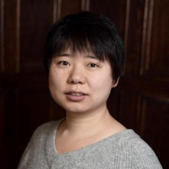 woman with short hair in a grey sweater in front of a dark wood wall